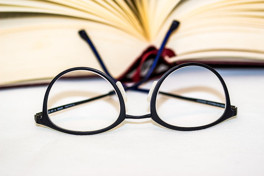 Black reading glasses on white surface with open book