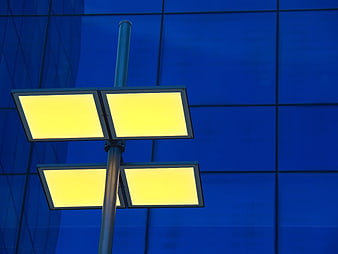 Yellow street lamp against blue glass building facade