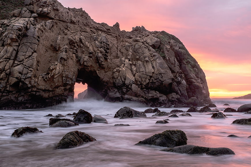 Dramatic coastal rock arch at sunset with long exposure ocean