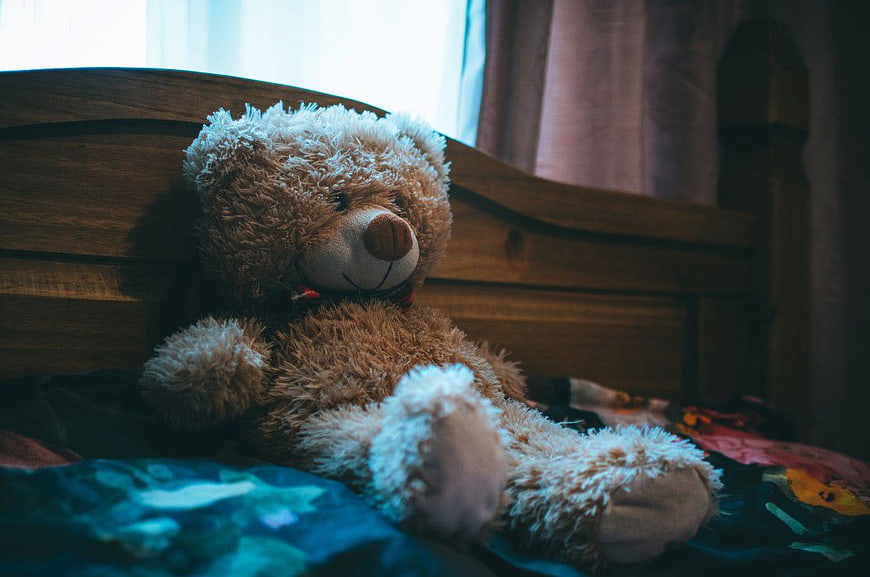 Cuddly brown teddy bear sitting on a bed