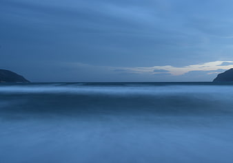 Serene Blue Ocean Landscape with Misty Waves and Distant Hills