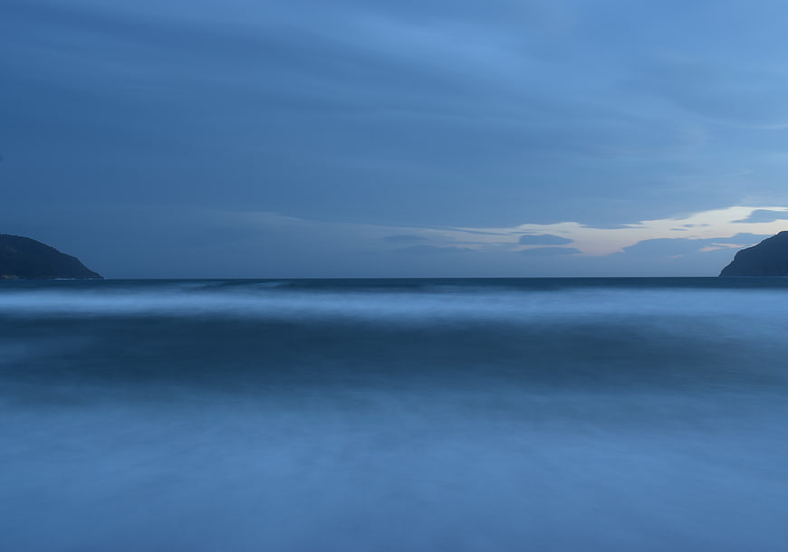 Serene Blue Ocean Landscape with Misty Waves and Distant Hills