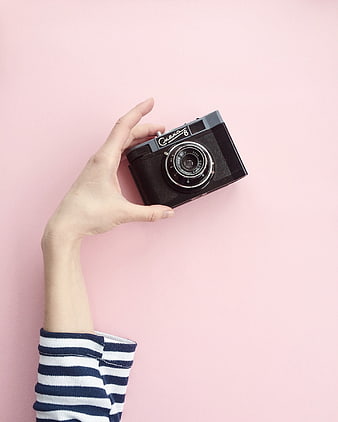 Hand holding vintage camera on pink background