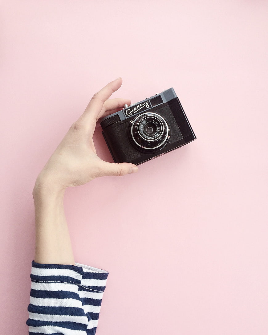 Hand holding vintage camera on pink background