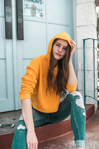 Young woman in yellow hoodie and ripped jeans sitting on porch