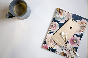 Flat lay of coffee mug, smartphone, and floral notebook on white desk