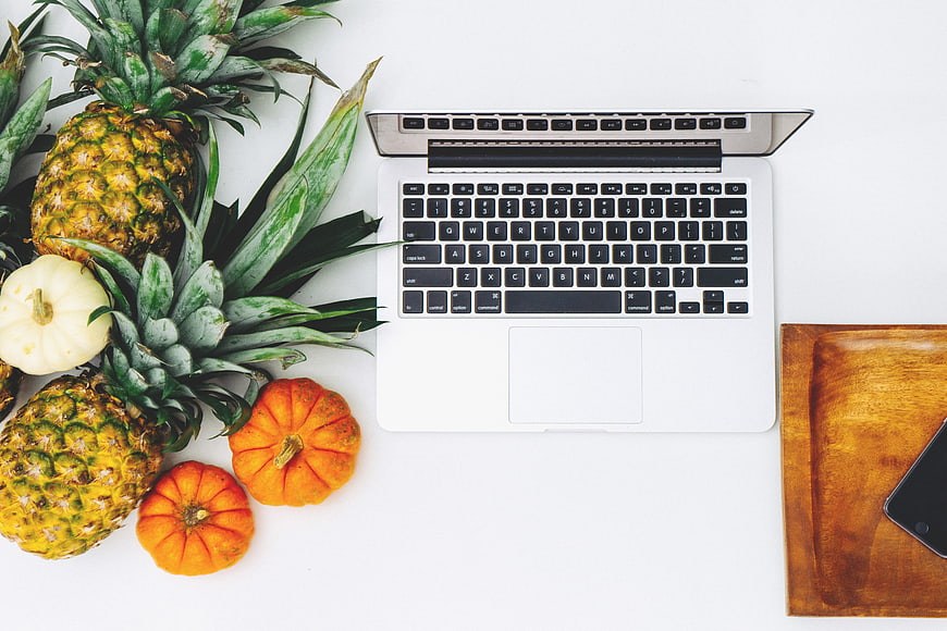 Flat lay of laptop, pineapples, and pumpkins on white desk