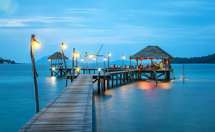Wooden pier with thatched roof restaurant at twilight