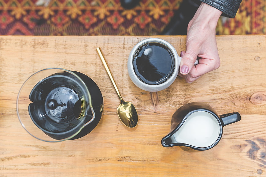 Top view of coffee cup, milk pitcher, and spoon on wooden table