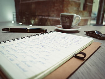 Handwritten notebook with pen and coffee cup on desk