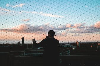 Silhouette of Man Behind Wire Fence at Sunset