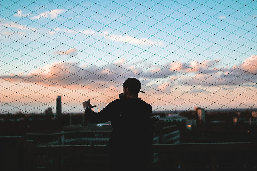 Silhouette of Man Behind Wire Fence at Sunset