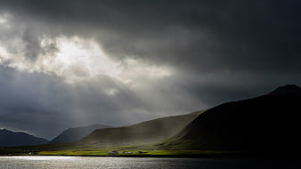 Dramatic Sun Rays Breaking Through Storm Clouds Over Mountain Lake