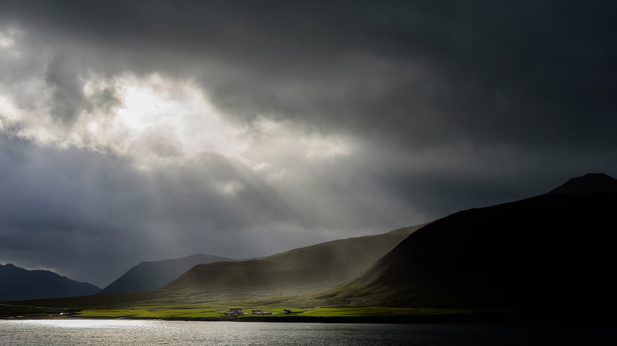 Dramatic Sun Rays Breaking Through Storm Clouds Over Mountain Lake