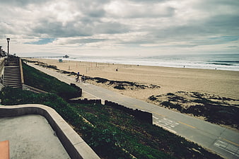 Wide coastal view with pier, beach, and cyclists on path