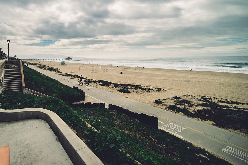 Wide coastal view with pier, beach, and cyclists on path