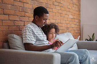 Father and daughter reading a book together on a couch