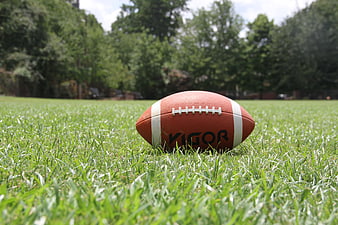 American football on green grass field with blurred trees