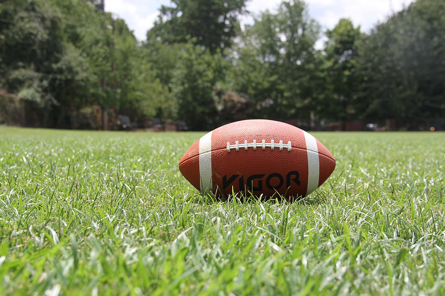 American football on green grass field with blurred trees