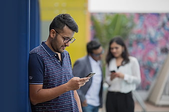 Man using smartphone outdoors with blurred colleagues