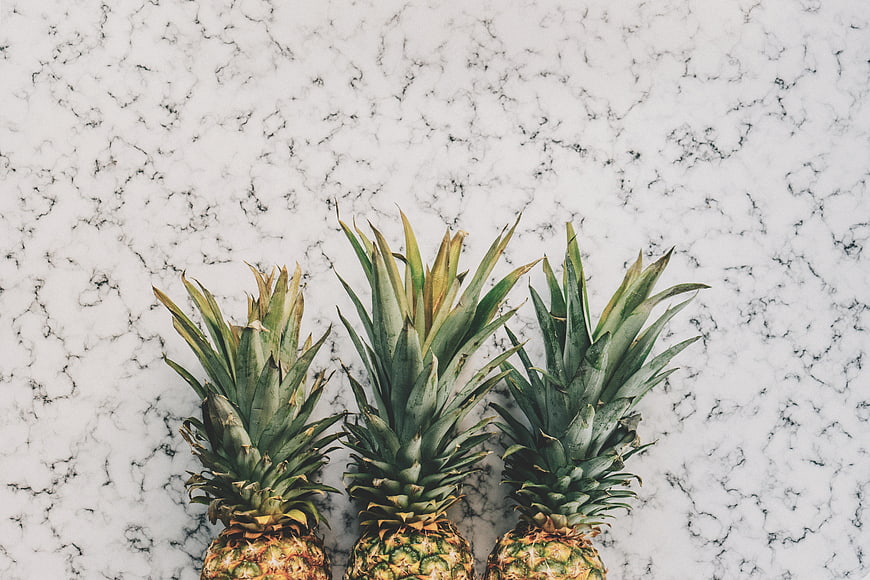 Three pineapples on white marble background top view