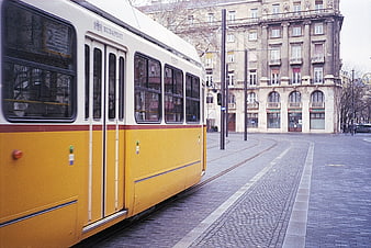 Yellow Budapest tram on cobblestone street with historic architecture