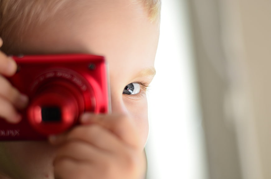 Close-up of child holding red digital camera to eye