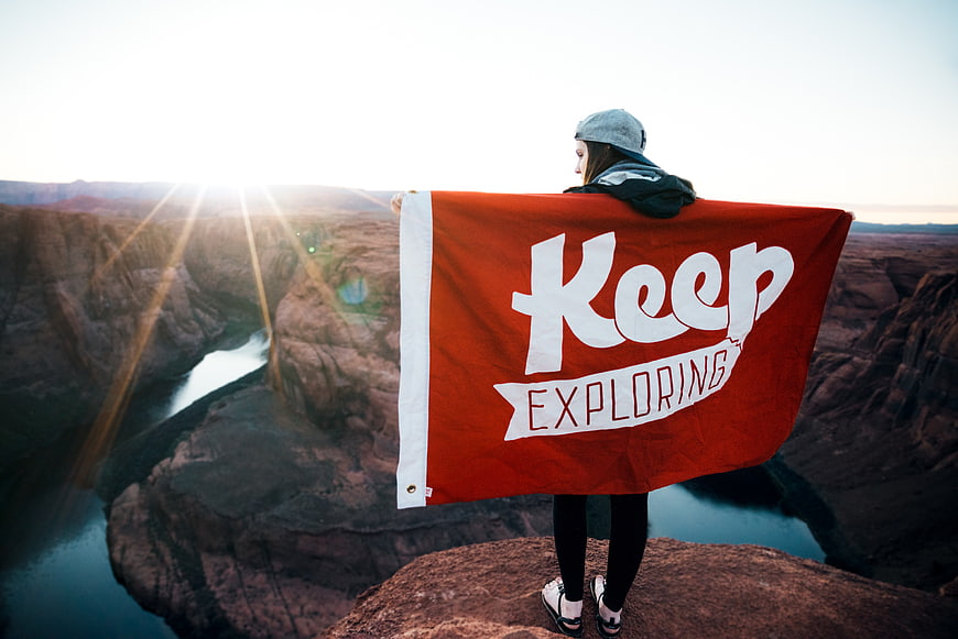 Woman holding Keep Exploring flag overlooking canyon river