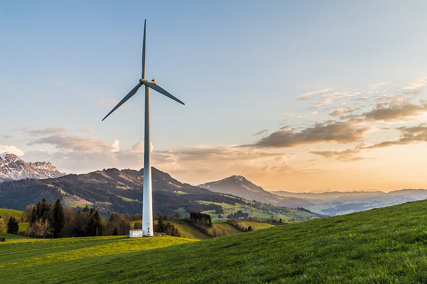 Wind Turbine on Green Hillside with Mountain Landscape at Sunset