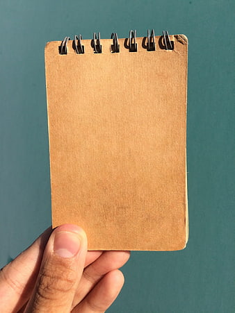 Hand holding brown spiral notebook against teal background