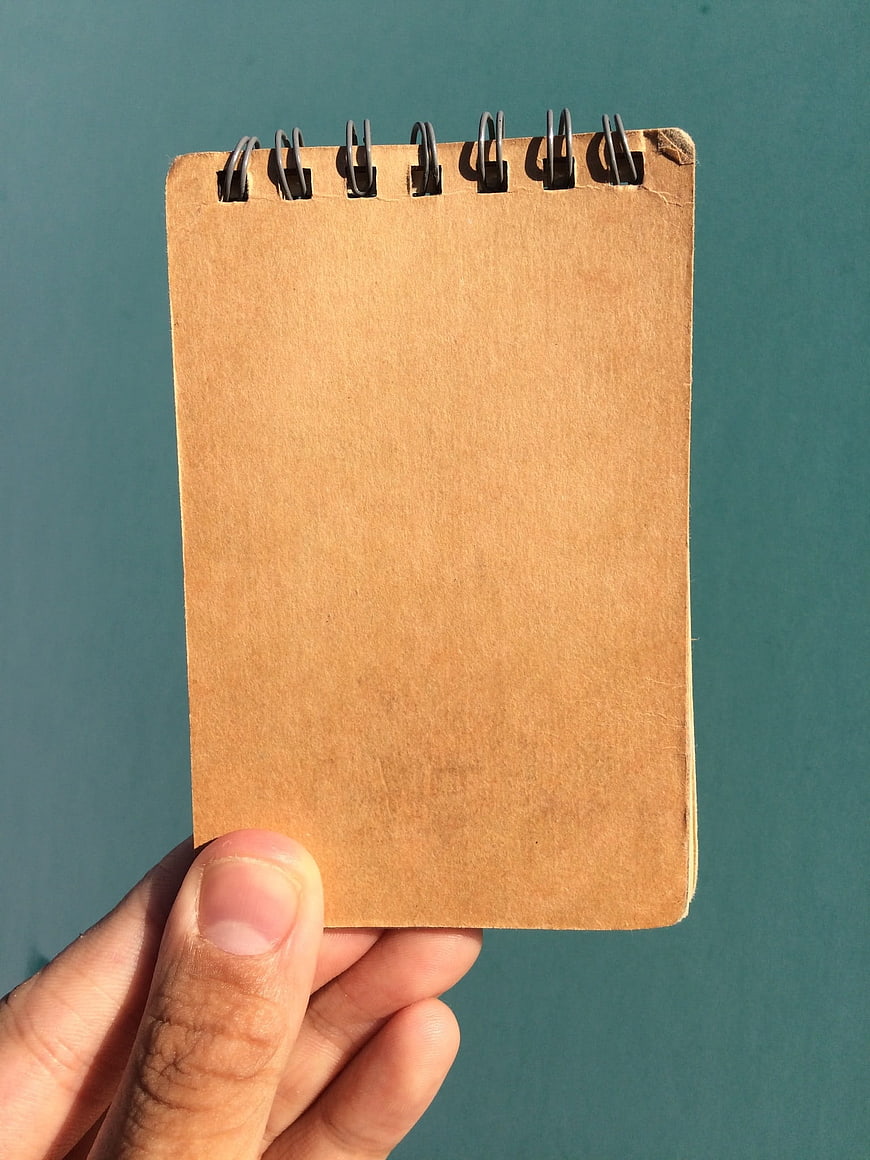 Hand holding brown spiral notebook against teal background