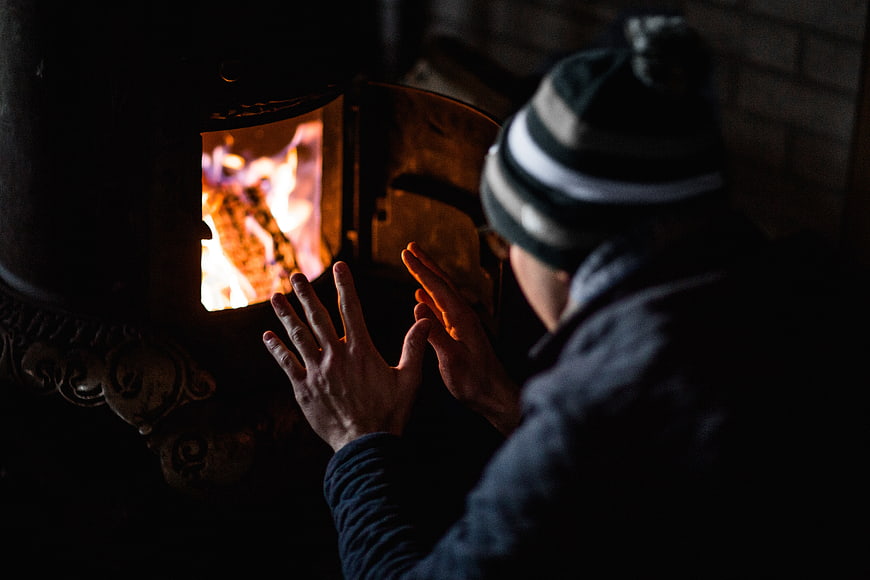 Man warming hands by wood stove fire in winter
