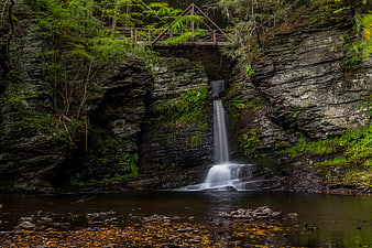 Serene Waterfall Cascading into Forest Pool with Wooden Bridge