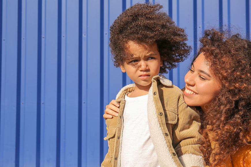 Mother holding grumpy child against blue wall