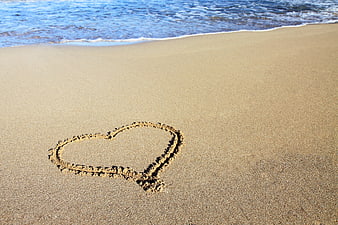 Heart drawn in sand on beach with ocean waves