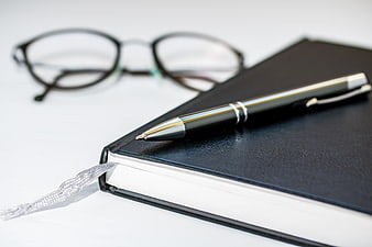 Black leather notebook with silver pen and reading glasses on white desk