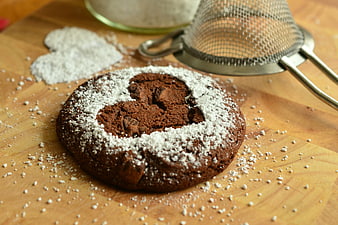Chocolate cookie with heart-shaped powdered sugar design on wooden board