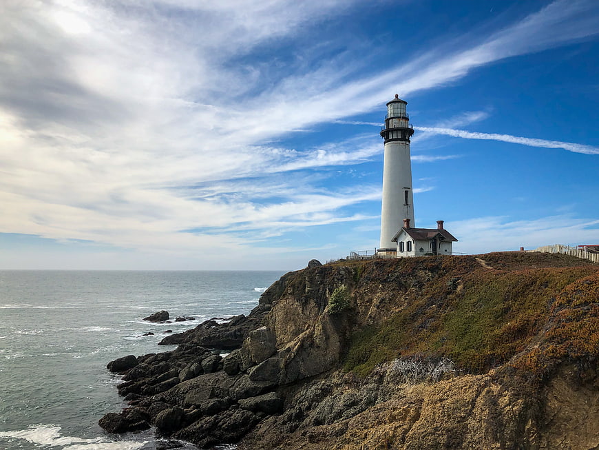 White Lighthouse on Rocky Coastal Cliff Under Blue Sky