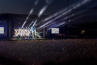 Wide shot of a live outdoor concert with dramatic stage lighting and a large crowd