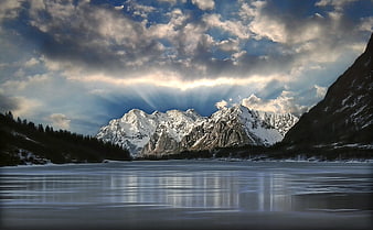 Dramatic Sunbeams Over Snow-Capped Mountains and Frozen Lake