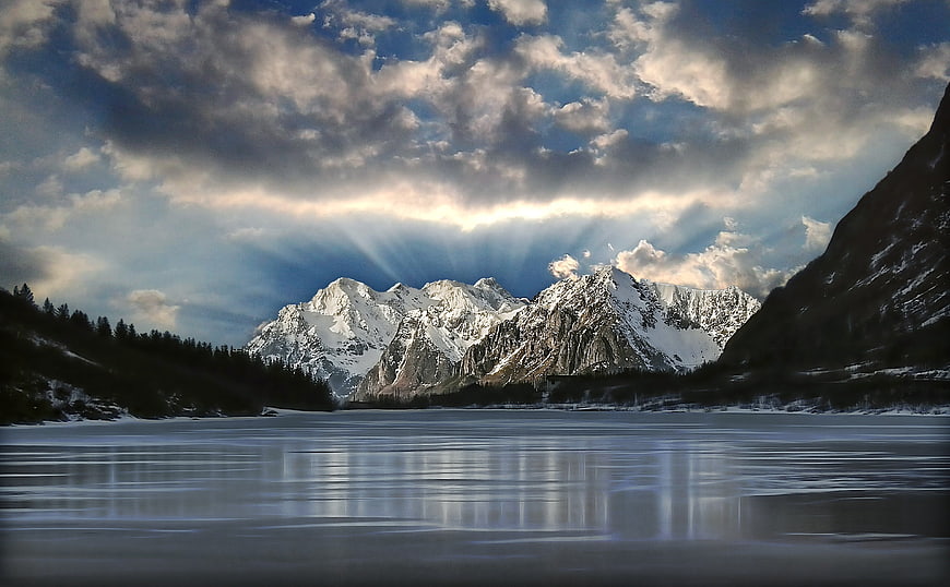 Dramatic Sunbeams Over Snow-Capped Mountains and Frozen Lake