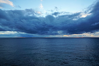 Dramatic dark storm clouds over calm blue ocean horizon