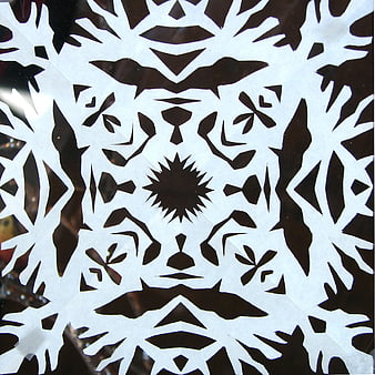 Symmetrical white paper snowflake pattern on dark background