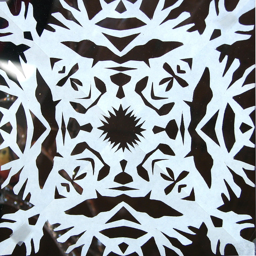 Symmetrical white paper snowflake pattern on dark background