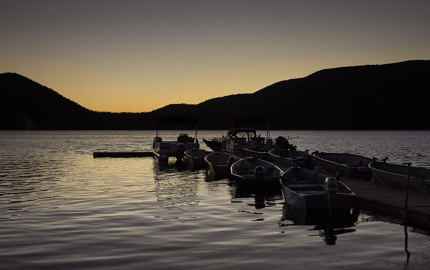 Silhouetted boats docked at lake during golden hour sunset