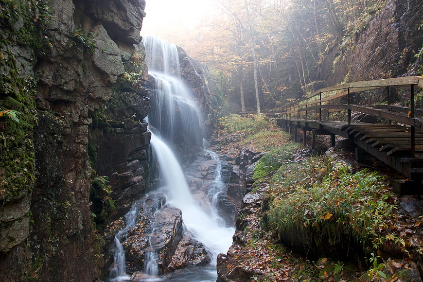 Serene Waterfall Cascading Beside Wooden Bridge in Autumn Forest