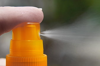 Close-up of finger pressing orange sunscreen spray bottle nozzle
