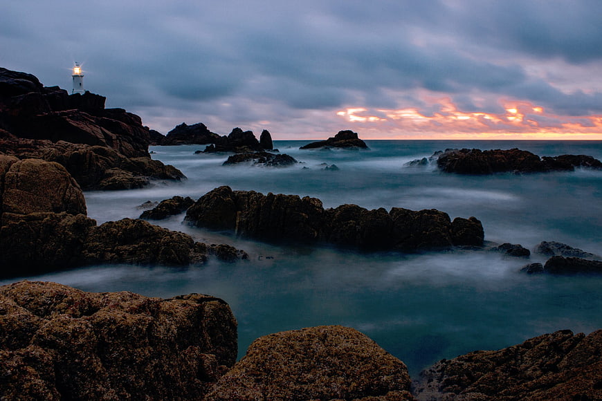 Lighthouse on Rocky Coast at Sunset with Long Exposure Waves