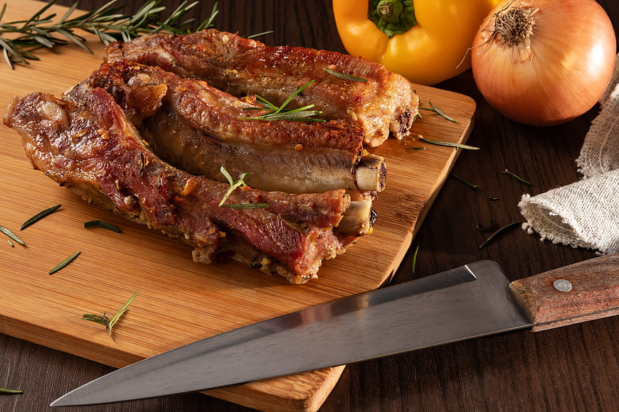 Roasted Pork Ribs on Wooden Board with Knife and Vegetables