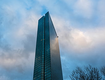 Low angle view of modern glass skyscraper against cloudy sky